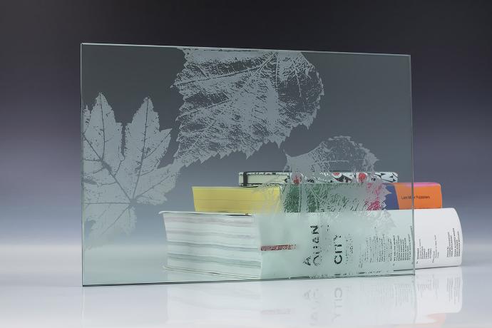 A square piece of etch glass with a floral pattern and books on a neutral background
